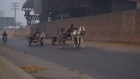A-horse-cart,-two-donkey-cars-and-a-motorcycle-on-the-road-in-winters`s-foggy-season,-Electric-polls,-wall,-sign-board-and-a-factory-with-the-road