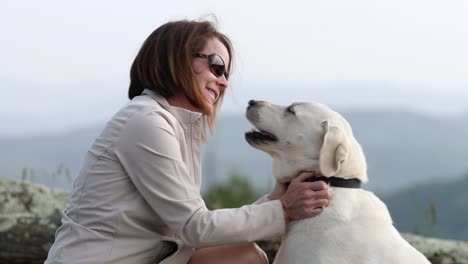 Woman-pets-white-lab-with-mountains-in-background