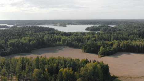 Aerial,-rising,-drone-shot-overlooking,-forests,-fields-and-a-lake,-on-a-misty-and-partly-sunny,-summer-day,-in-Kirkkonummi,-Uusimaa,-Finland