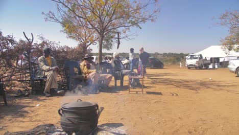 Zwei-Botswana-Männer-Sitzen-Tagsüber-Mit-Dampfendem-Topf-Am-Feuer