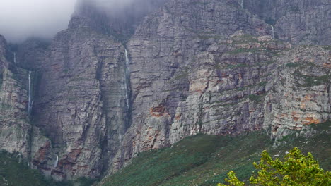 Multiple-waterfalls-falling-down-mountain-side-after-heavy-rains,-zoomed-in-panning-shot