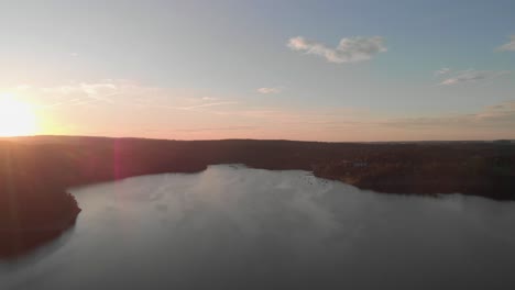 Eine-Professionell-Aussehende-Luftaufnahme-Eines-Sees-In-Rosa-orangefarbenem-Sonnenuntergang,-Der-Direkt-Auf-Die-Sonne-Zufliegt