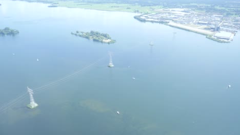 An-aerial-view-of-a-lake-in-Europe,-The-Netherlands-with-green-nature,-an-island,-cell-tower-masts-and-a-town-in-the-frame