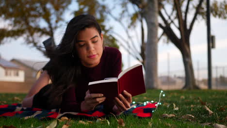 A-beautiful-young-hispanic-woman-opening-the-pages-of-a-story-book-or-novel-and-reading-in-the-park-in-autumn-SLIDE-RIGHT