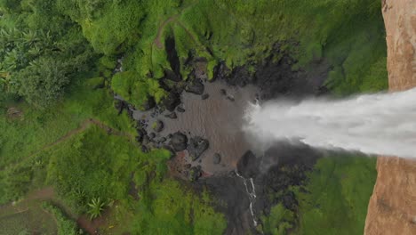 A-moving-forward-aerial-birds-eye-view-shot-of-a-waterfall-in-rural-Uganda-plunging-over-the-edge-of-a-cliff-into-a-deep-pool