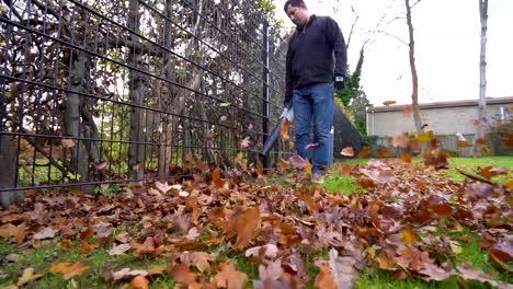 Messy-fall-leaves-blown-in-a-cloudy-day-by-gardener-using-leaf-blower-in-slow-motion