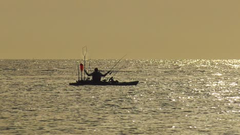 Woman-Sea-fishing-from-a-kayak-on-calm-sea-at-dawn,-silhouette-slow-motion