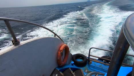 View-from-back-of-boat-looking-over-the-wake-from-boat-with-rescue-life-buoy,-railing-and-steps-in-4K