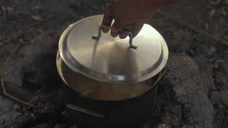 Refugee-lifts-off-lid-cooking-food-refugee-camp