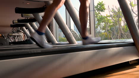 Sportliche-Männerbeine,-Die-Auf-Laufband-Im-Fitnessraum-Mit-Fensterglas-Und-Gartenhintergrund-Laufen