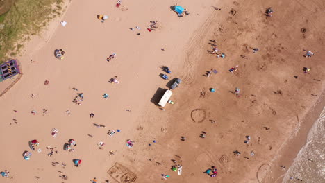 Aerial-Rotation-of-Beach-Goers-Relaxing-in-the-Sunshine-on-a-Golden-Sandy-Beach