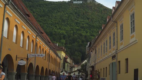 Upwards-tilt-of-The-Houses-in-Council-Square-Revealing-the-Brasov-Sign-while-tourist-enjoy-the-day-in-Brasov,-Romania