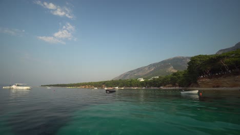 Kleine-Boote-Vor-Der-Küste-Kroatiens-In-Klarem,-Türkisfarbenem-Wasser-Mit-Sanften-Hügeln,-Die-Sich-Zu-Einem-Blauen-Himmel-Erheben