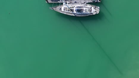 Top-down-aerial-view-of-sailing-boats-and-yachts-moored-on-the-turquoise-waters-of-Brighton-Marina,-UK-a-push-over-the-jetty-with-people