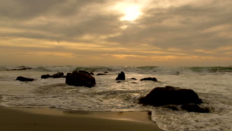 Kleine-Wellen-Rollen-über-Kleine-Felsen-Am-Strand-Bei-Schönem-Sonnenuntergang-Und-Dramatischem-Himmel,-Goldene-Stunde