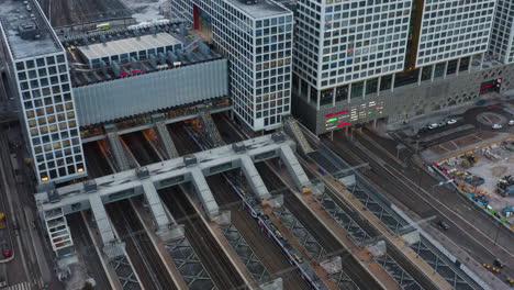 Aerial,-static,-drone-shot-of-trains-and-traffic,-in-front-of-the-Mall-of-Tripla-shopping-center,-and-the-Pasila-railway-station,-on-a-partly-sunny-evening,-in-Helsinki,-Finland