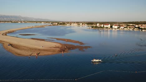 Aerial-panorama-of-a-Nin-town,-sandy-beach,-lagoon-and-boat-approaching-in-sunset