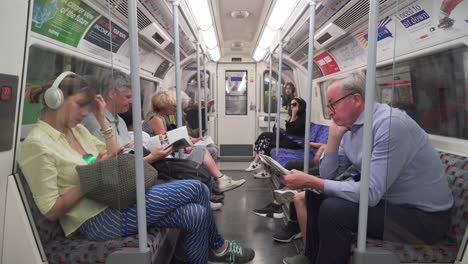 Older-man-entering-London-underground-train,-sitting-down-and-reading-newspaper