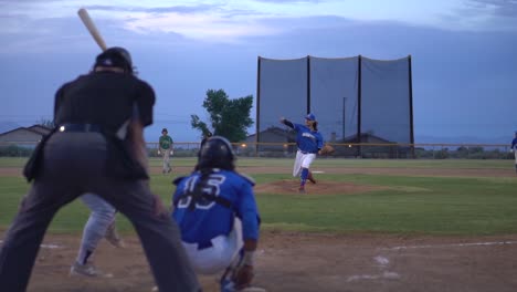 Slow-motion-clip-during-minor-league-baseball-game-from-behind-home-plate-during-pitch-and-hit,-panning-on-runner-on-the-way-to-first-base