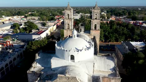 Aerial-closeup-pulling-back-from-the-towers-of-the-Catedral-de-San-Gervasio-revealing-the-full-depth-of-the-church-in-Valladolid,-Yucatan,-Mexico-just-after-sunrise