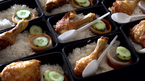 A-row-of-Nasi-Lemak-with-Chicken-Roasted-in-lunch-boxes-container-while-hands-put-a-plastic-spoon-with-it