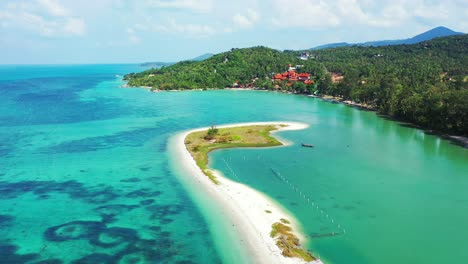 Touristic-village-on-coastline-of-tropical-island-with-lush-vegetation-in-front-of-calm-turquoise-lagoon-surrounded-by-white-sandy-stripe-in-Koh-Phangan,-Thailand