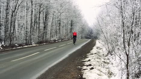 Stable-shot-showing-behind-perspective-of-ciclyst-going-through-snowy-forest-on-an-empty-road