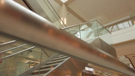 Stairs-with-glass-barriers-and-chrome-railings-in-large-shopping-mall-looking-up-to-large-skylights