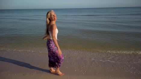 Pretty-mature-woman-smiling-and-walking-along-a-beach-dressed-in-a-sarong-and-looking-very-happy
