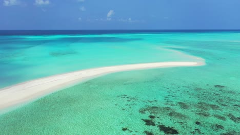 Long-narrow-sandy-stripe-surrounded-by-calm-clear-water-of-turquoise-lagoon-with-coral-reef-on-a-blue-ocean-horizon-in-Maldives
