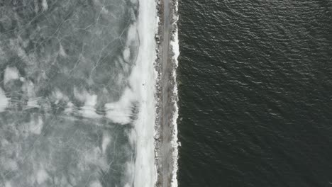 Top-down-drone-shot-of-a-path,-with-ice-on-the-one-side-and-water-on-the-other