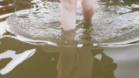 White-legged-girl-steps-into-muddy-water,-walks-through-water-approaching