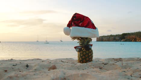 Strand-In-Curaçao---Ananas-Mit-Weihnachtsmütze-Und-Sonnenbrille-Am-Sandstrand-Bei-Sonnenuntergang---Nahaufnahme