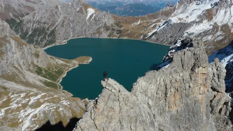 Rotierende-Drohnenaufnahme-Eines-Mannes,-Der-Nach-Einer-Langen,-Intensiven-Und-Extremen-Wanderung,-Um-Den-Gipfel-Des-Berges-Zu-Erreichen,-Auf-Einer-Klippe-Mit-Blick-Auf-Den-Love-Heart-Lake-In-Der-Schweiz-Steht