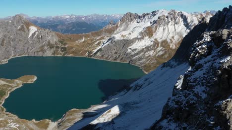 Luftaufnahme-Eines-Mannes,-Der-Am-Rand-Einer-Kleinen-Und-Schmalen-Klippe-Steht-Und-Nach-Einer-Extremen-Wanderung-Zum-Gipfel-Des-Berges-Die-Atemberaubende-Landschaft-Vor-Sich-Am-Lünersee-In-Der-Schweiz-überblickt