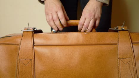 Hands-holding-brown-suitcase-medium-shot