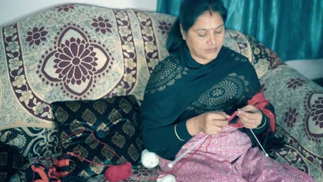 Traditionelle-Indische-Frau,-Die-Mit-Roter-Wolle-Und-Zwei-Nadelhandwerken-Strickt,-Die-In-Einem-Bett-Sitzen