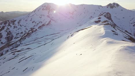 Schöne-Luftaufnahme-Von-Schneebedeckten-Bergen,-Während-Die-Sonne-über-Dem-Berggipfel-Untergeht