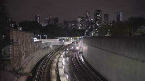 A-DLR-train-station-and-train-leaving-in-London-during-a-clear-night-with-buildings-of-canary-wharf-in-the-background