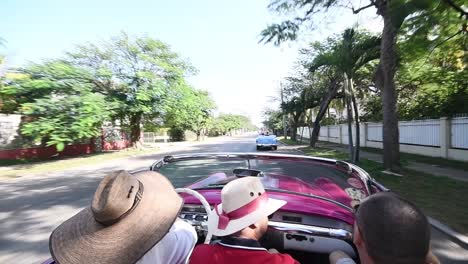 Amigos-Conduciendo-Por-Las-Calles-De-La-Habana-Durante-Un-Día-Soleado-Con-Un-Viejo-Coche-Tradicional-Cabrio-Rojo-De-Cuba