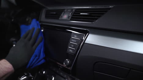 Static-close-up-4k-shot-of-a-male-hand-in-a-black-rubber-glove-cleaning-and-polishing-a-luxurious-car-dashboard-and-dashboard-computer-using-a-blue-rag