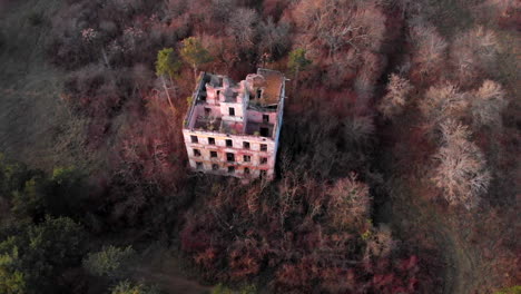 Old-abandoned-gunpowder-factory-building-in-the-woods-in-autumn,-tilt-down-aerial