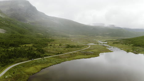 Un-Coche-Que-Viaja-Por-La-Carretera-Cerca-Del-Tranquilo-Lago-Y-La-Cordillera-De-Hemsedal,-Noruega
