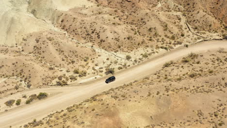 Dark-black-SUV-drives-slowly-down-a-dirt-road-passed-a-dirt-pullout-in-the-middle-of-a-dry-and-desolate-desert