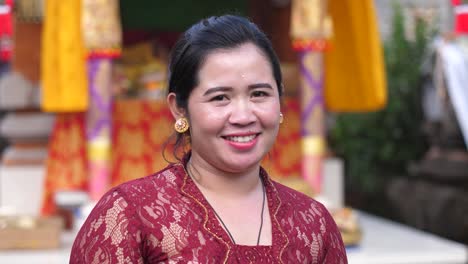 Mujer-Feliz-Con-Vestido-De-Encaje-Rojo-Oscuro-Parada-Frente-A-Coloridas-Cortinas-Y-Pancartas-En-El-Templo-Hindú-En-Bali