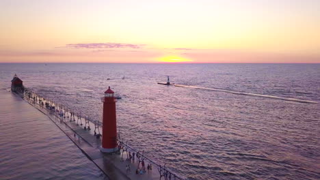 Aerial-shot-of-large-boat-passing-by-Grand-Haven-Lighthouse-at-sunset