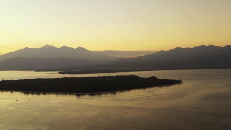 Gili-Islands,-Beautiful-misty-sunrise-over-the-calm-sea-water,-small-islands-and-mountains-in-the-background