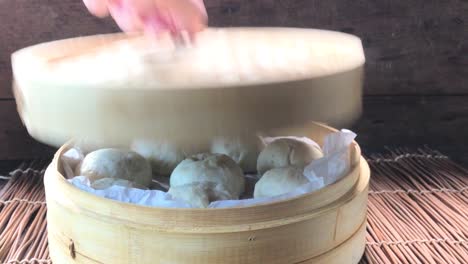 three-quarter-view-of-uncovering-lid-of-cooked-steamed-buns-showing-steam-rising