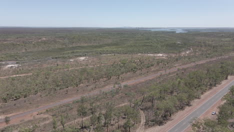 Aerial-moving-drone-shot-of-Highway-and-railway-with-Darwin-City-in-the-distance-in-Northern-Territory,-Australian-Outback
