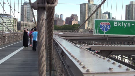 Tourists-Walk-Across-the-Brooklyn-Bridge,-Cars-on-Highway-Below